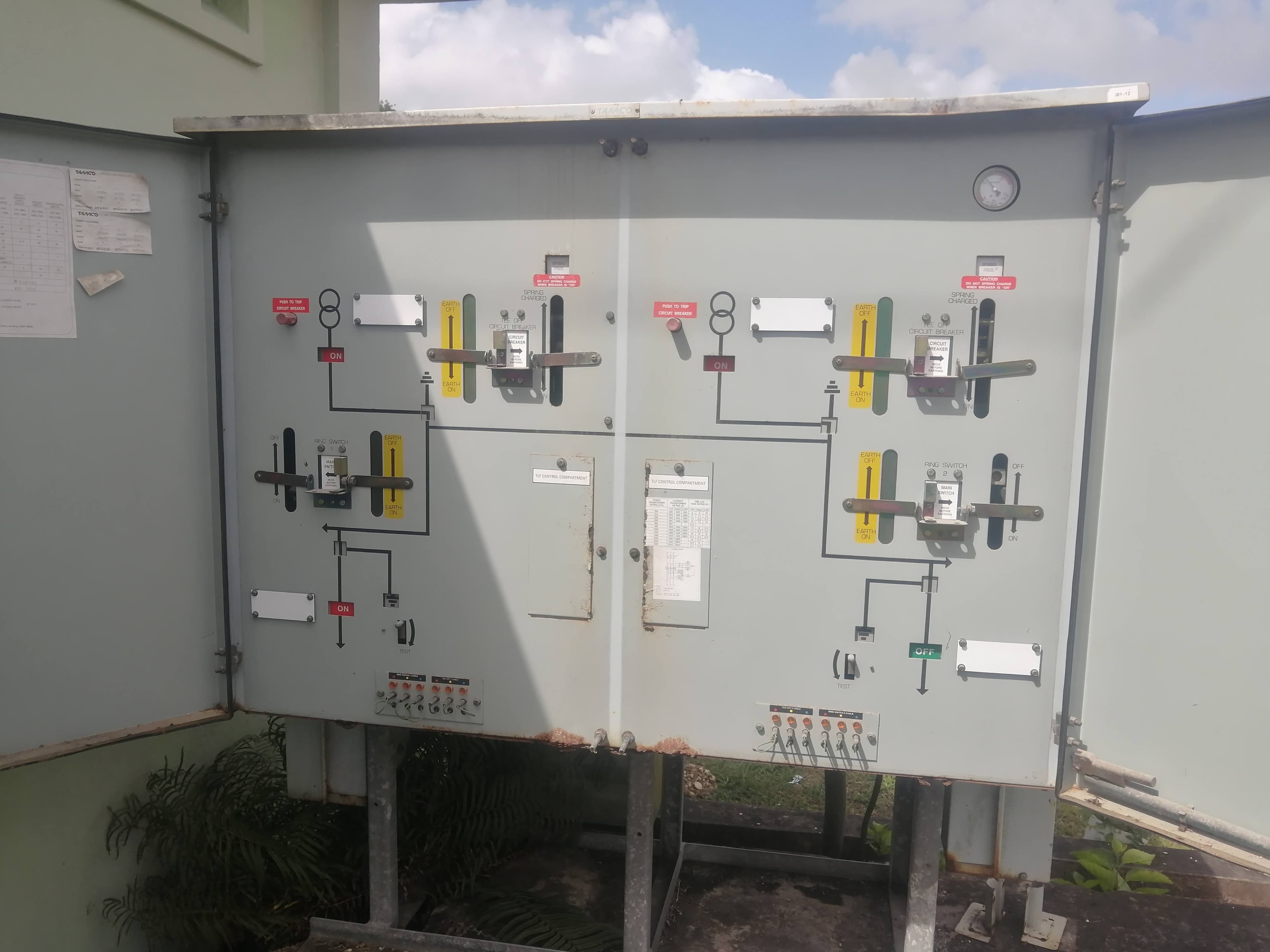Outdoor electrical control panel with open doors revealing various switches, levers, and technical diagrams.