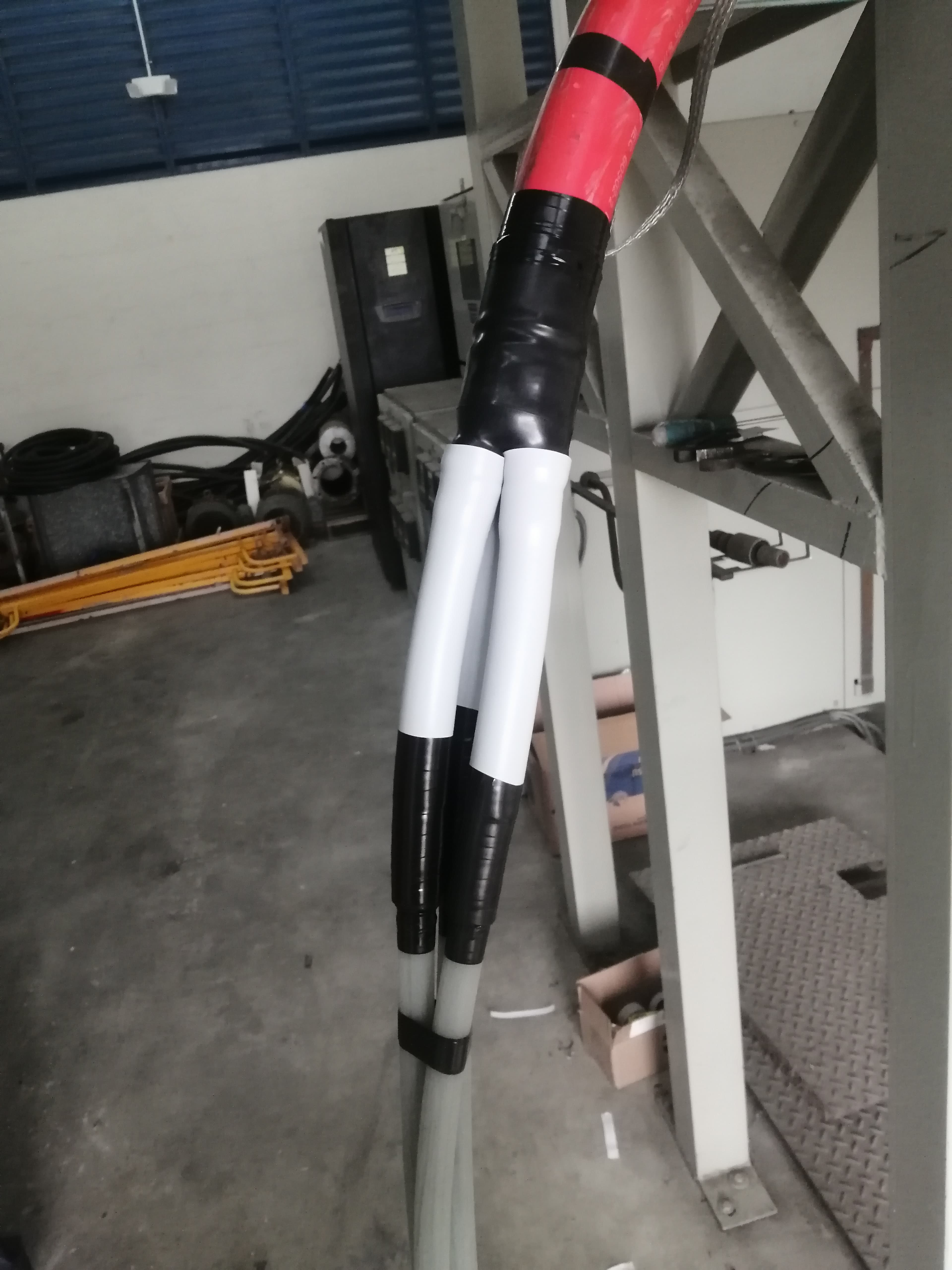 Thick red industrial cable splitting into two white cables secured with black tape and insulation.