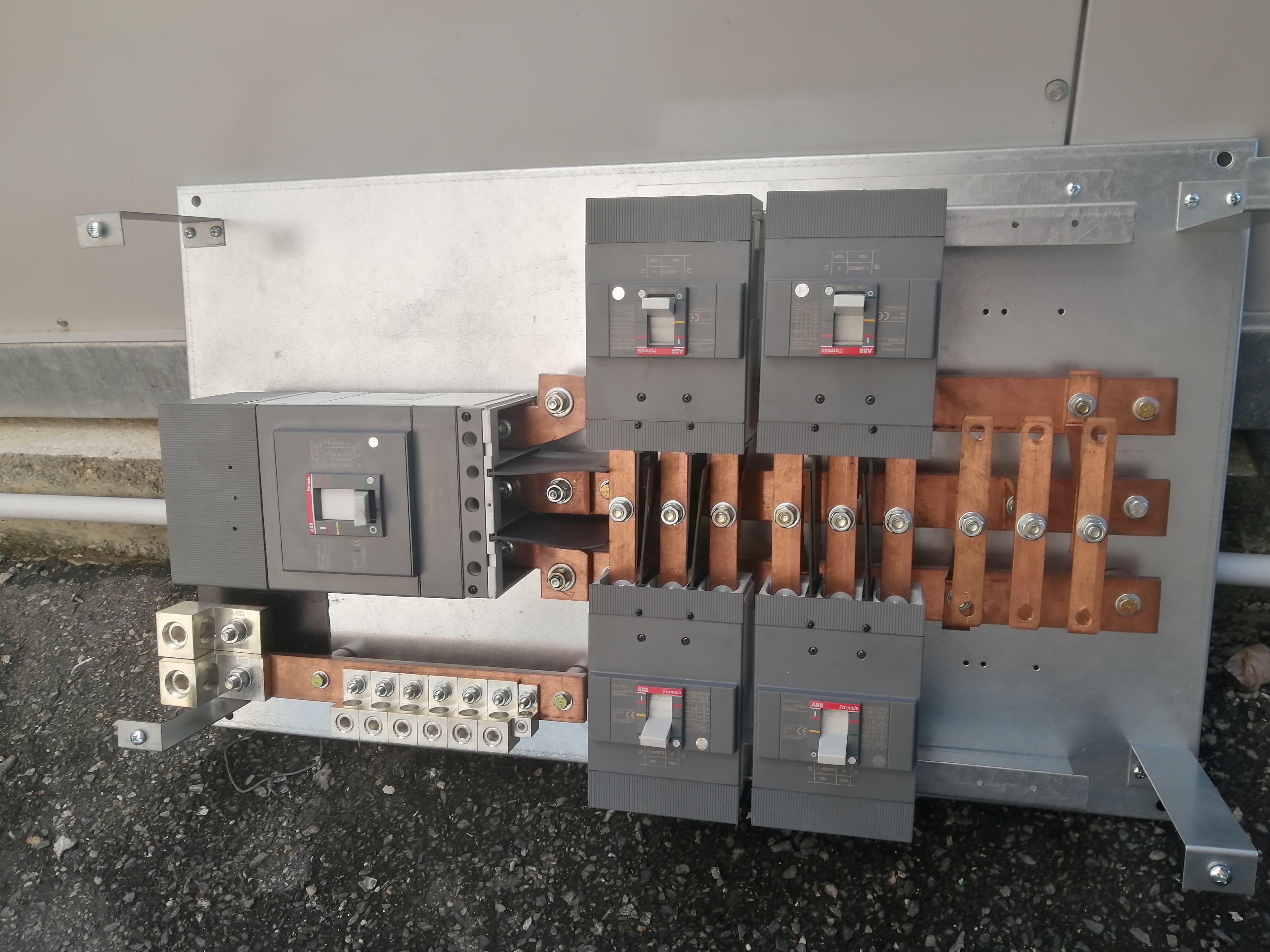 Grey ABB circuit breakers and copper busbars mounted on a silver metal electrical panel assembly.