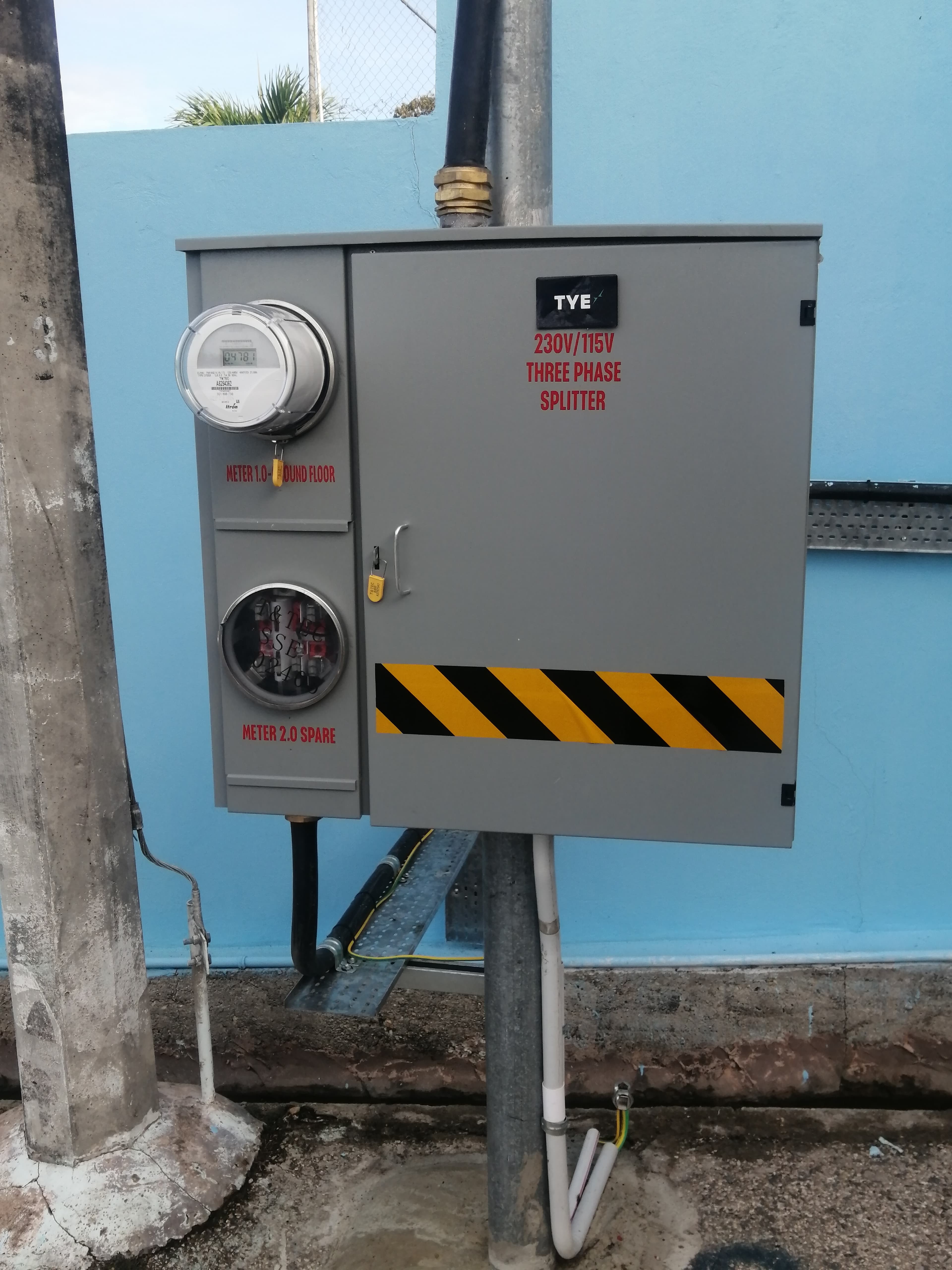 Gray electrical box with a digital meter, three-phase splitter label, and yellow hazard stripes.